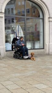 Ich sitze mit Luna vor der Touristeninformation. Man erkennt den platten Rollstuhlreifen.