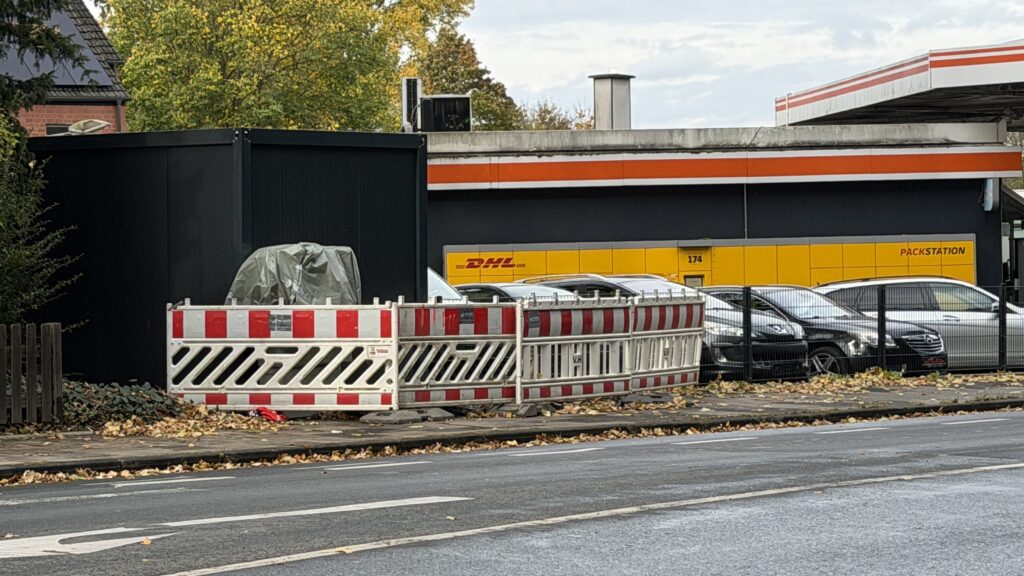 Baustellen-Absperrung nach Verrücken der Füße; von gegenüberliegender Strassenseite fotografiert; im Hintergrund ist die Packstation und die Tankstelle zu sehen